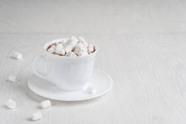 Soğuk kış ve sonbahar günlerinde ahşap zeminde servis edilen kar gibi görünen kremalı sıcak kakao içeceğiyle dolu beyaz bir fincan. Kopyalama alanı olan resim, yatay