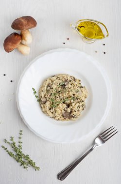 Mantar, kekik, beyaz şarap, zeytin yağı ve beyaz ahşap zemin üzerinde çatalla servis edilen parmesan peyniri içeren İtalyan kremalı risotto arborio pirinç tabağının en üst görüntüsü. Dikey yönelim