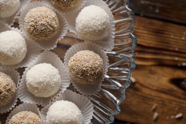 Hindistan cevizi ve vejetaryen enerji topu şekerlemelerinin üst görüntüsü beyaz zanaat kağıdında cam kekin içinde sabahları mutfakta, siyah ahşap masada duruyor. Yatay yönelim resmi