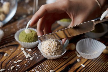 Gümüş bıçaklı, organik vejetaryen fındık toplarını dilimleyen, beyaz el işi kağıt üzerinde, siyah ahşap masa üzerinde, tatilde mutfakta ayçiçeği tohumları olan bir el. Yatay yönelim resmi