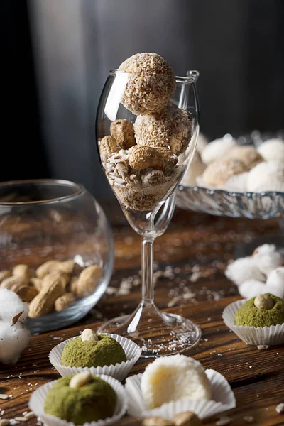 Vegetarian nut energy ball candies made of sunflower seeds served in drinking glass standing on dark wooden table with bowl of peanuts at party on holiday. Vertical orientation image