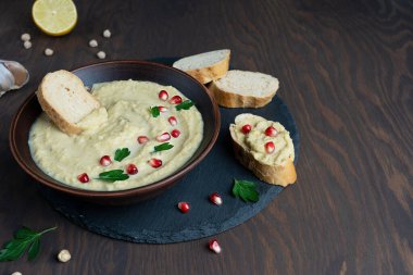 Tahinili nohut, limon suyu ve nar tohumlarıyla süslenmiş sarımsak ve ekmek dilimli yuvarlak tepside maydanozdan yapılmış humus aromalı yemek. Tahta arka planda. Kopyalama alanı olan resim