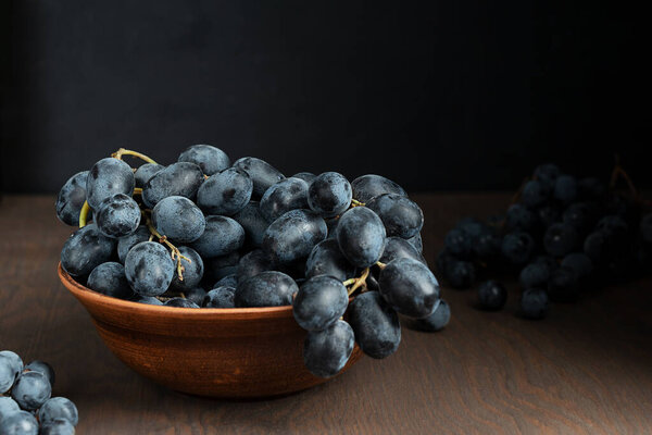 Куча красного винограда лежит в коричневой глиняной чаше на темном деревянном фоне на кухне, показывая уборку осеннего сезона в винограднике. Горизонтальное изображение ориентации