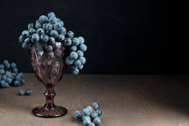 Isabella ya da Tib üzümleri, üzüm bağındaki hasat sezonu partisini gösteren kahverengi ahşap arka planda mor oyulmuş şarap kadehlerine asılmış. Kopyalama alanı olan resim, yatay