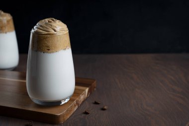 Hazır kahve tozu, şeker ve sıcak suyla yapılan ev yapımı modaya uygun dalgona kahvesi. Koyu tahta arka planda buzlu sütle servis ediliyor. Kopyalama alanı olan resim