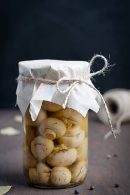 Tek cam kavanoz dolusu ev yapımı organik marine edilmiş ya da mayalanmış mantarlı siyah ahşap arka planda siyah biber ve körfez yapraklarıyla mutfakta. Dikey yönelim resmi