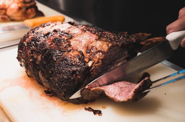 Şef büyük bir parça eti beyaz bir kesme tahtasıyla dilimliyor.