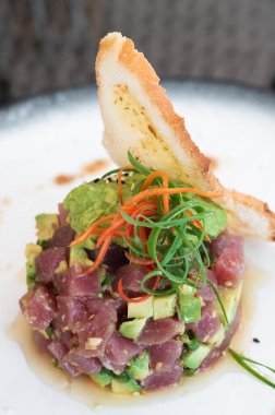 Çiğ ton balığı ve avokado salatası beyaz bir tabakta çıtır ekmekle servis edilir..