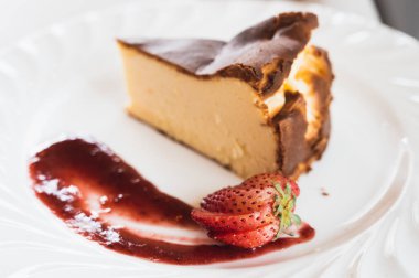 Beyaz tabakta çilek soslu Bask peynirli kek.