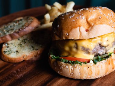 Sarımsaklı ekmek ve patates kızartmasıyla servis edilen etli peynirli burger. Yemek teslimatı.