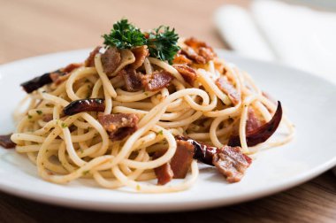 Pastırmalı spagetti, kırmızı biberli, sarımsaklı, yuvarlak, beyaz bir tabakta, peçeteli.