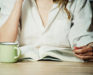 Kız kitap okuyor ve yakın planda kahve içiyor.