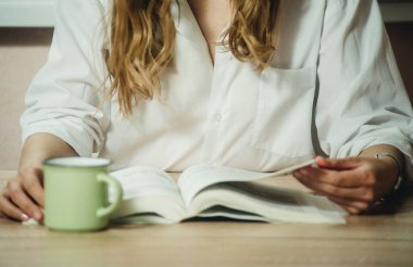 Kız kitap okuyor ve yakın planda kahve içiyor.