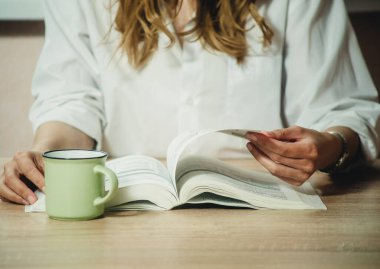 Kız kitap okuyor ve yakın planda kahve içiyor.