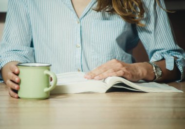 Kız kitap okuyor ve yakın planda kahve içiyor.