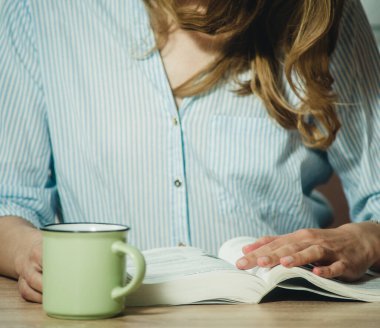 Kız kitap okuyor ve yakın planda kahve içiyor.
