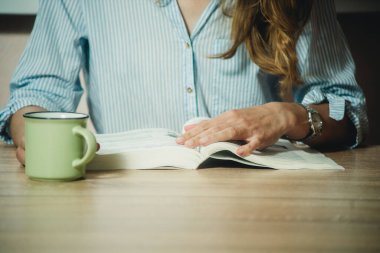 Kız kitap okuyor ve yakın planda kahve içiyor.