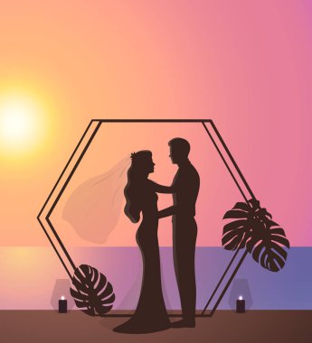 Tropik Plaj Düğün Konsepti. Günbatımında Monstera Leaves and Candles ile süslenmiş romantik bir çift. Güzel yeni evliler birbirlerine bakıyor, deniz kenarında sarılıyorlar..