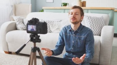 Young man blogger shooting video of himself using camera on tripod, content creation for social media, modern technology and blogging freelance work concept