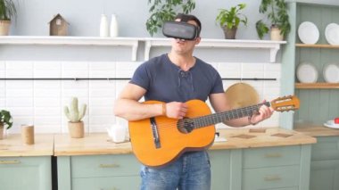 Gitar çalan heyecanlı genç adam evde sanal gerçeklik kulaklığı kullanıyor, yavaş çekim.
