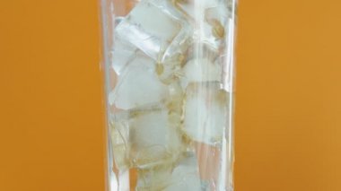 Turuncu bir arka plan üzerinde cam içine buz küpleri ile kola soda Dökme