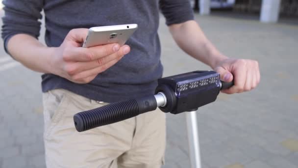 Primer plano del hombre usando su teléfono inteligente mientras está de pie en la calle con scooter eléctrico, pagando en línea — Vídeos de Stock