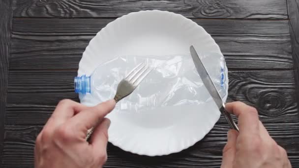Bouteille en plastique froissée sur plaque et mains mans avec couverts, concept de pollution plastique, vue de dessus — Video