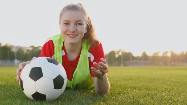 Retrato de una adolescente futbolista sonriente acostada en el campo con pelota de fútbol en cámara lenta — Vídeos de Stock