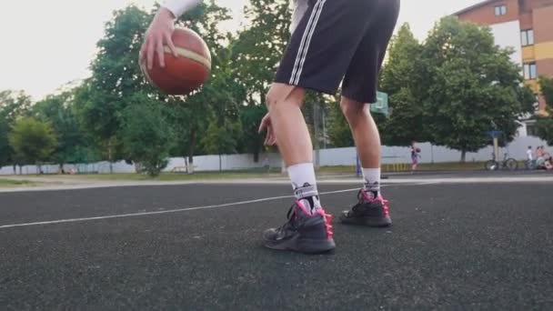 Un joven en la cancha de baloncesto goteando con pelota. Entrenamiento de Streetball — Vídeo de stock