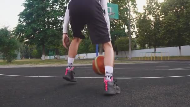 Primer plano del joven en la cancha de baloncesto goteando con pelota . — Vídeo de stock