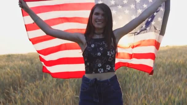 Retrato de una chica americana excitada sosteniendo la bandera de Estados Unidos sobre el campo de trigo. Movimiento lento — Vídeos de Stock