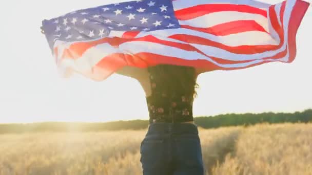 Американская девочка-подросток машет американским флагом США "Звезды и полосы" на пшеничном поле на закате — стоковое видео