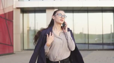 Gözlüklü ve telefonda konuşan iş kadınacele. Stresli ve meşgul kadınlar. Arka planda modern iş binası