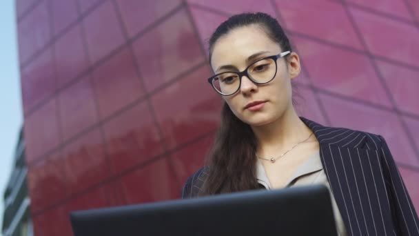 Porträtt av säker affärskvinna som arbetar med laptop, modern byggnad som bakgrund — Stockvideo
