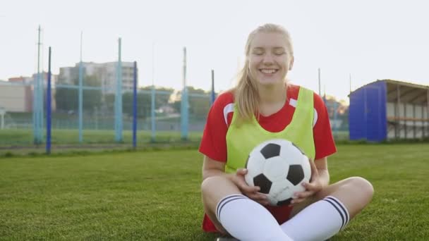 Πορτραίτο ενός χαμογελαστή έφηβος κορίτσι ποδοσφαίρου κάθεται στο γήπεδο με μπάλα ποδοσφαίρου — Αρχείο Βίντεο