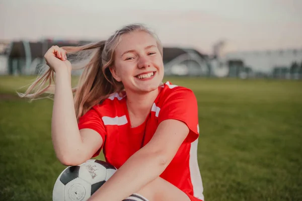 Portrét usmívající se dívky fotbalista s fotbalovým míčem sedí na trávě — Stock fotografie