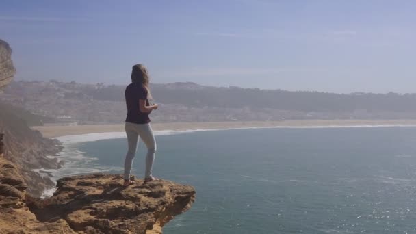 Jonge vrouw staat op de top van de rots en kijkt naar de kust in de zomer — Stockvideo