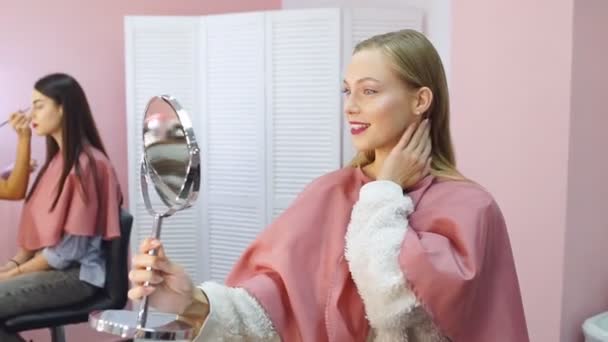 Mosolygó fiatal nő ügyfél néz egy kézi tükör után a smink eljárás. — Stock videók