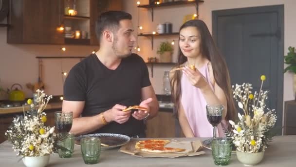 Evde romantik bir akşam yemeği yerken pizza yiyip kırmızı şarap içen mutlu ve tutkulu bir çift. Sevgililer Günü konsepti — Stok video
