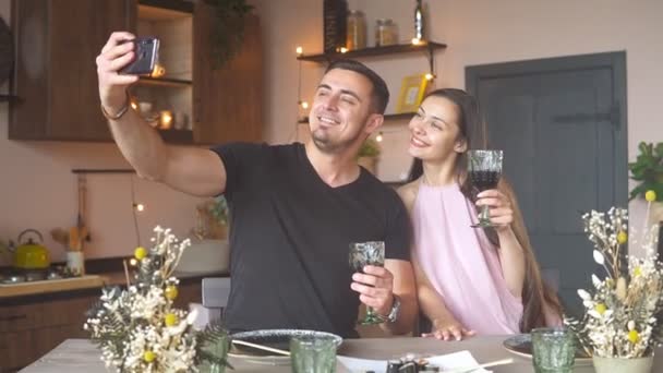 Güzel genç bir çift ellerinde şarap kadehleriyle selfie çekiyor ve evde kutlama yaparken gülümsüyor. — Stok video