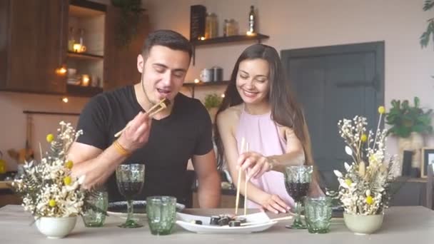 Šťastný vášnivý pár jíst sushi a pít červené víno z brýlí při romantické večeři doma — Stock video