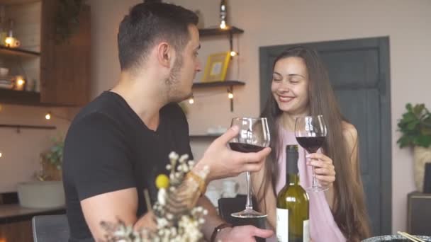 Mladý milující pár slaví speciální událost s červeným vínem. Dívají se jeden druhému do očí s láskou a smíchem. — Stock video