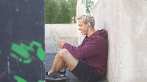 Спортивный человек, используя свой смартфон на перерыве от тренировки в городской спортивной площадке, замедленной съемки — стоковое видео