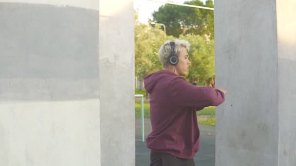 Fitness muž zahřívá venku na sportovním hřišti a poslouchat hudbu ve sluchátkách. Otočí tělo a houpe rukama — Stock video