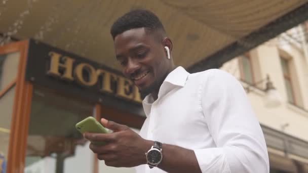 Otelin dışında duran akıllı telefonunu kullanan Afrikalı Amerikalı bir adam. — Stok video
