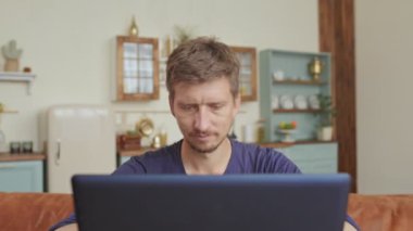 Kafkasyalı adam boş vakitlerini kanepede geçiriyor ve modern evde dizüstü bilgisayar kullanıyor. Gençlerin mobil cihazlardan hoşlanması kavramı