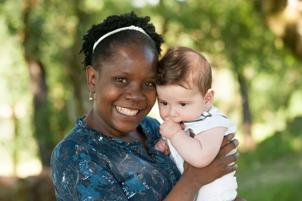 African mom holding her caucasian baby in nature. Great copy space.