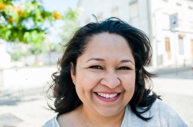 Latin Amerikalı bir kadının kameraya mutlu bir şekilde bakışının ön planı.