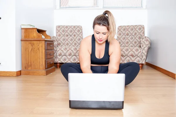 现代生活 一个身材高大的女人坐在地板上准备在家里开始她的网上健身课 — 图库照片