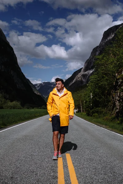 A tourist in a yellow raincoat walks along the highway